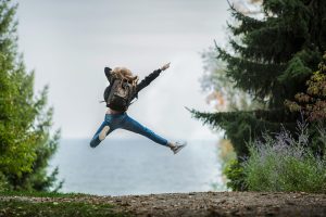 Energetic woman leaping in outdoor forest setting with lake view, showcasing freedom and joy after a hocatt ozone therapy session in dallas